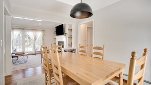 Ein Essbereich mit Holztisch und -stühlen, einer Pendelleuchte und einem Fernseher im Hintergrund.