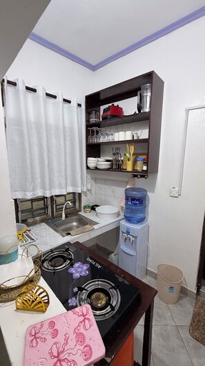 Una cucina compatta con fornello a gas, dispenser d'acqua e ripiano con utensili da cucina.