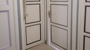 Un passadís amb dues portes tancades, cadascuna amb un disseny rectangular senzill i una manilla. El terra està emblenquat i les parets són de color blanc amb detalls blaus clars.