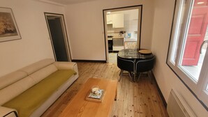 Espai vital compacte amb un sofà, una taula de dinar petita i una cuina visible a través d'una porta oberta.