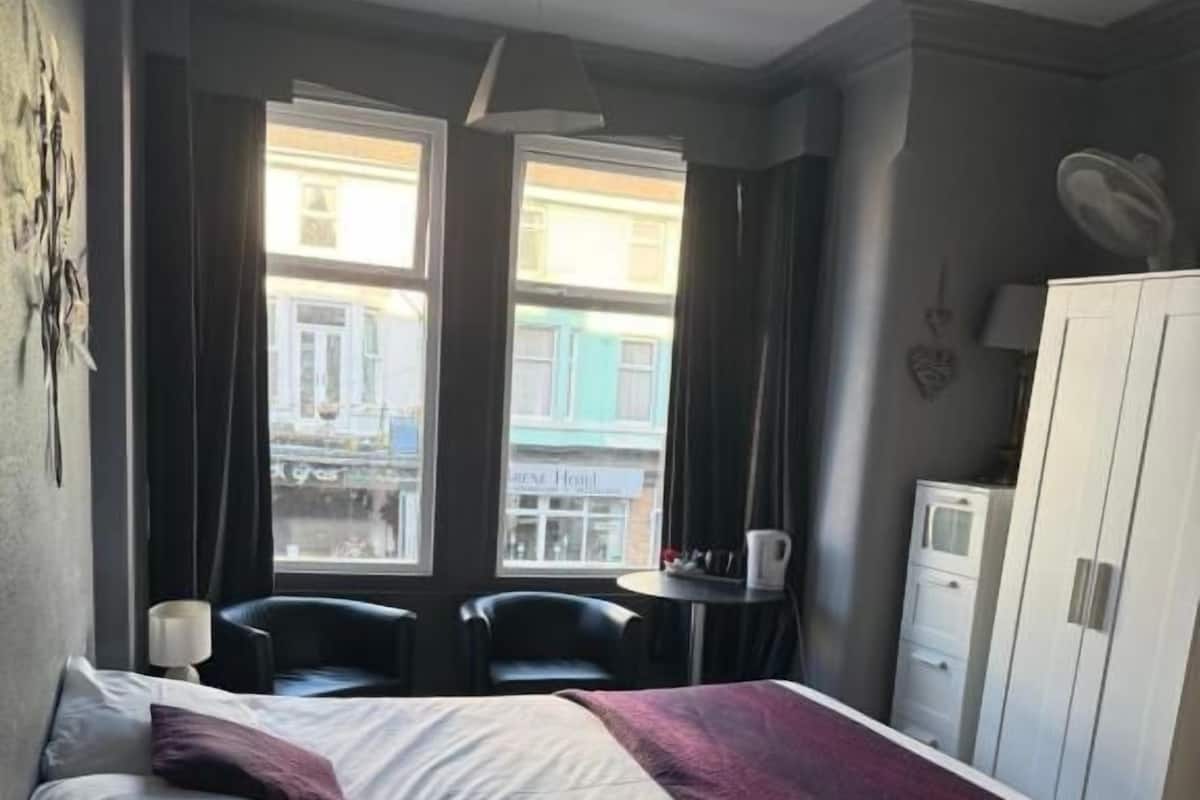 A hotel room with a bed, two chairs, a desk, and a wardrobe.