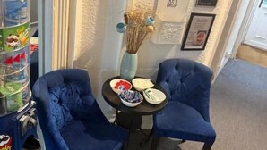 Ein Zimmer mit zwei blauen Stühlen, einem kleinen Tisch mit Schalen und einer Vase sowie einem Automaten.