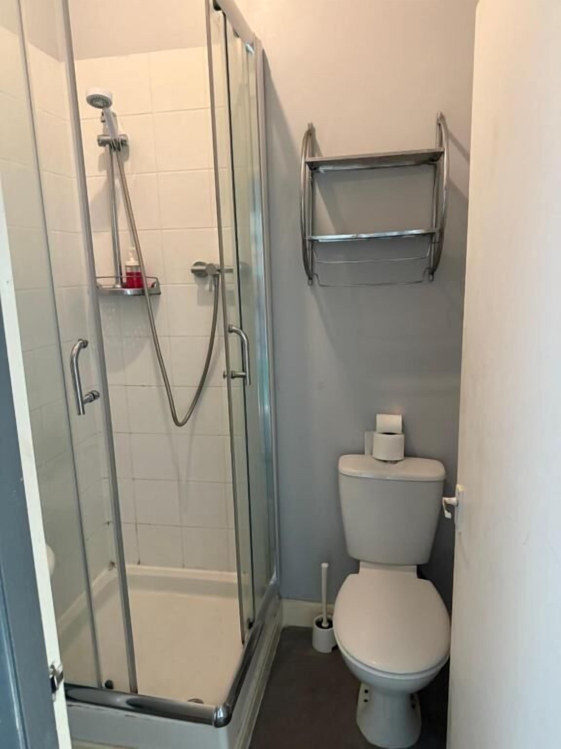 A small bathroom with a glass-enclosed shower, a toilet, and a shelf above the toilet.