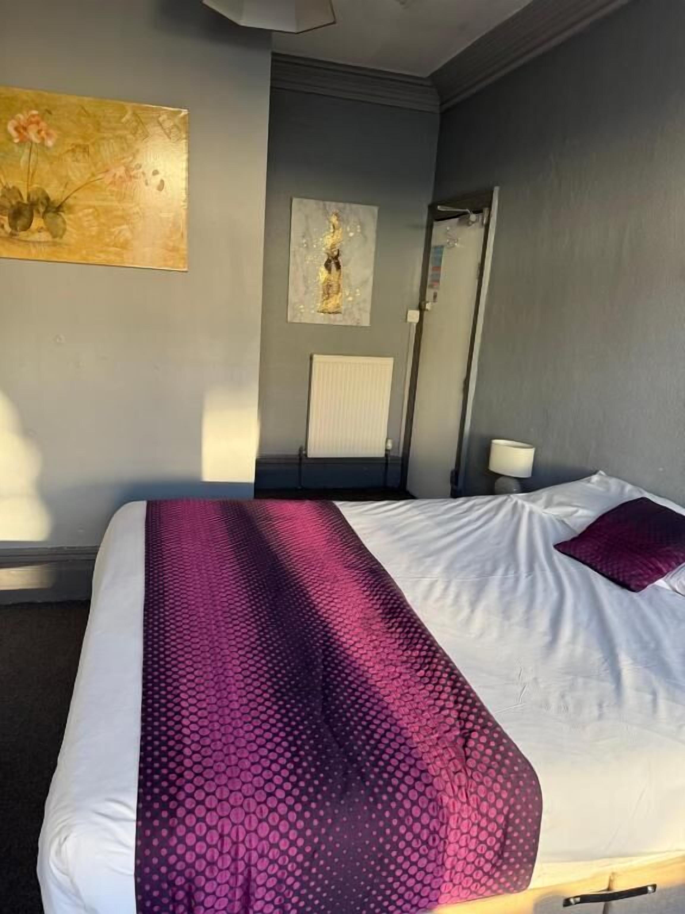 Habitación de hotel con cama, mesita de noche, una obra de arte en la pared y un radiador.