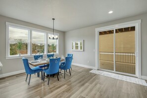 Comedor con mesa de madera, sillas azules y ventanas amplias con vistas a árboles.