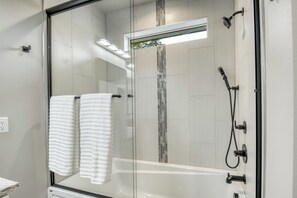 Un box de ducha moderno con puerta de cristal, un cabezal de ducha de mano, un grifo empotrado en la pared y un perchero con dos toallas.