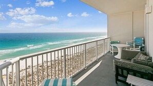 Een balkon met uitzicht op de oceaan, een witte tafel en groene, gestreepte stoelen.
