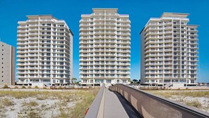 Een strandhotel met drie hoge gebouwen, een promenade die naar het strand leidt en een zandstrand.