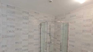 Ein Badezimmer mit einer gläsernen Duschkabine, einer weißen Badewanne und Wandfliesen mit Muster.