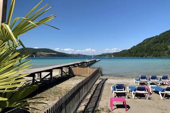 A beach with a wooden pier, clear blue water, and a row of beach chairs.