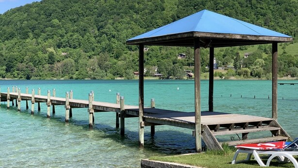 Een houten steiger die in een meer uitloopt, met een kiosk met een blauw dak aan het einde.