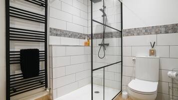Un baño moderno con ducha envuelta en vidrio, toallero negro, inodoro y salpicadero de azulejos.