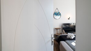 Een slaapkamer met een bed, een televisie, een wandlamp en een deur.