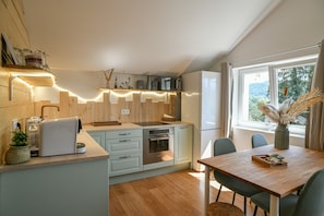 A modern kitchen with wooden cabinets, a built-in oven, and a dining area with a wooden table and chairs. - Gîte Les Collines with Garden and Private Jacuzzi (Villages du Lac de Paladru)