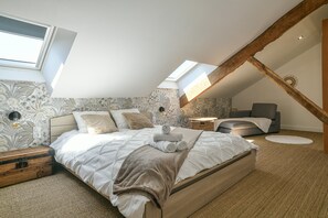 Ein Schlafzimmer mit geneigter Decke, einem Bett mit aufgerollten Handtüchern, einem Nachttisch und einer Wandlampe.