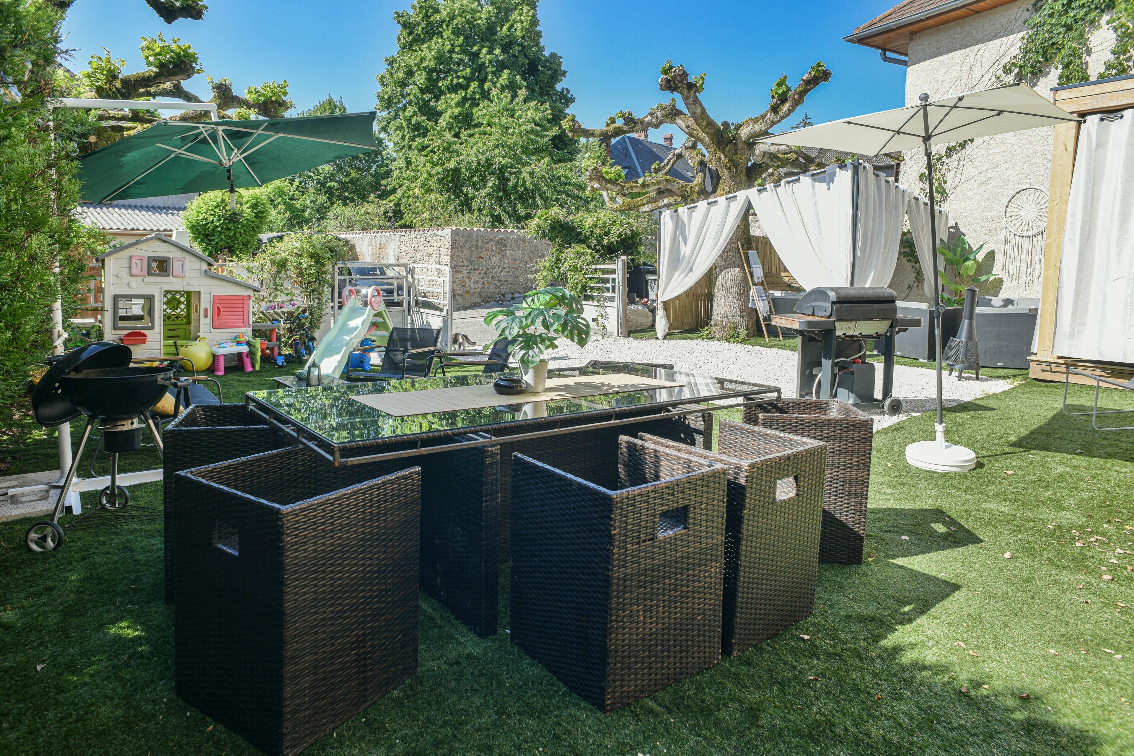 A backyard with a glass-top table, wicker furniture, a grill, and a play area.