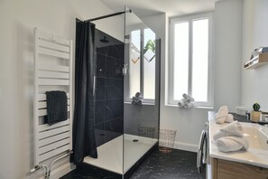 Ein modernes Badezimmer mit einer gläsernen Duschkabine, einem weißen Handtuchwärmer, einem Fenster mit Aussicht und einem Waschbecken mit Handtüchern.