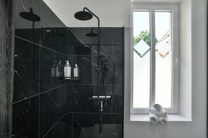 Ein modernes Badezimmer mit einer schwarzen Marmerdusche, einem Fenster mit Blick und ordentlich gefalteten Handtüchern am Fensterbrett.