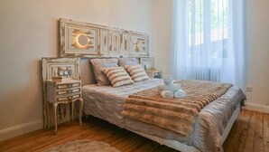 Un dormitorio con piso de madera, una cama con manta a rayas, una mesita de noche y un reloj en la pared.