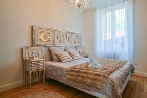 A bedroom with a wooden floor, a bed with a striped blanket, a bedside table, and a wall-mounted clock.