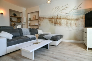 A modern living room with a sectional sofa, a coffee table, a flat-screen TV, and a wall mural.