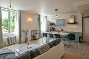 A modern kitchen with a central island, a dining area with a white table, and a living room with a sofa.