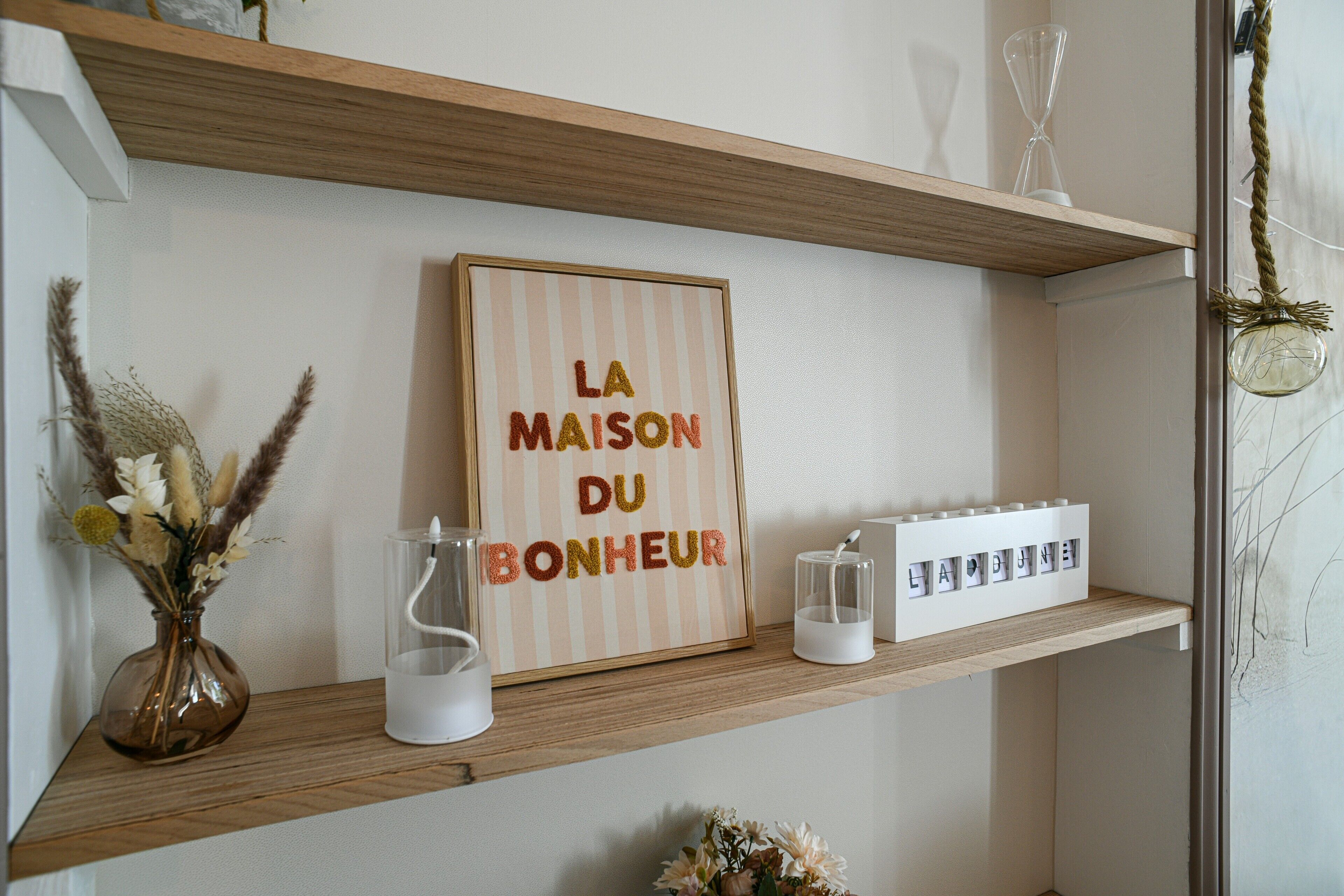 A shelf with a framed sign, a vase with dried flowers, and a white container.