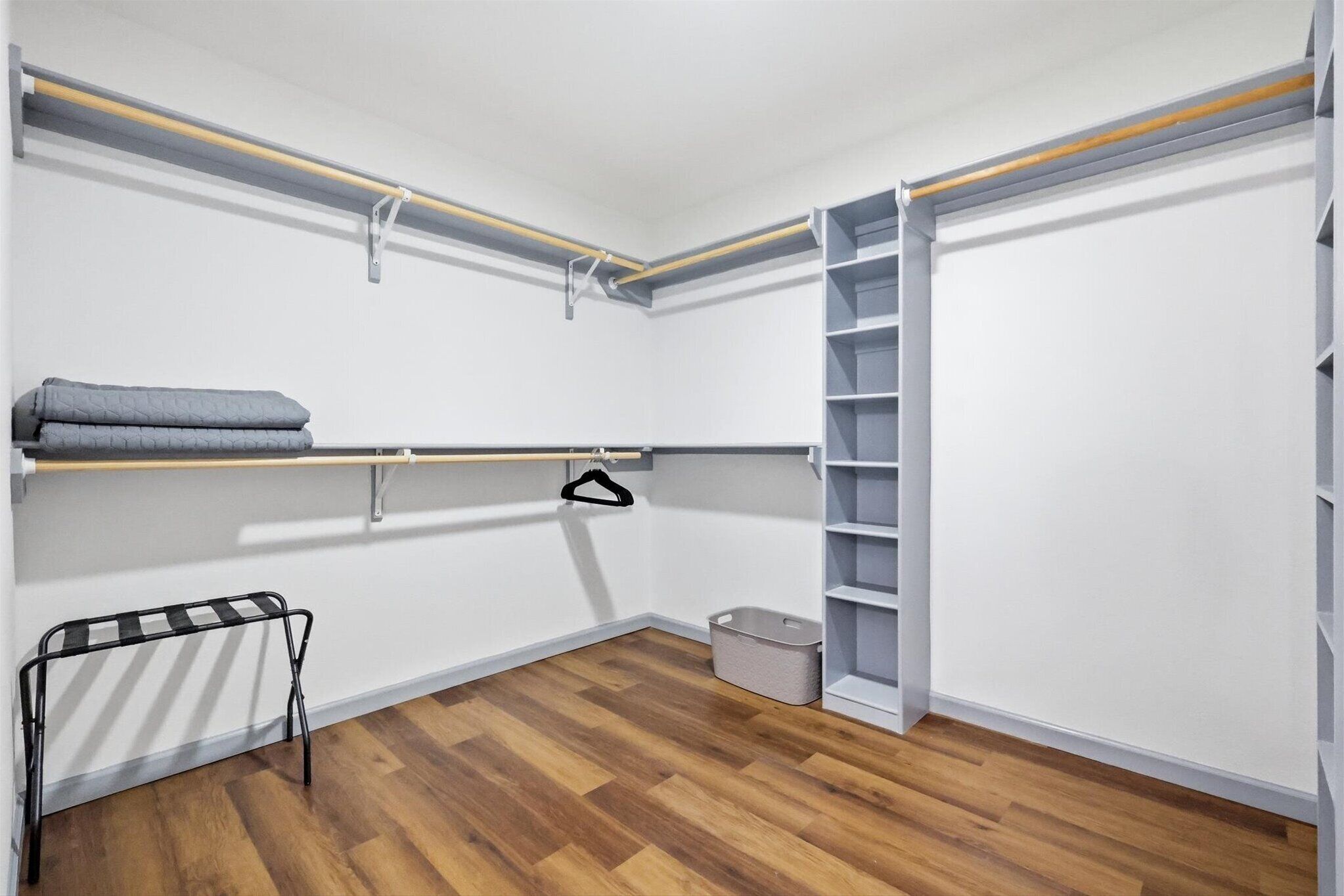 A walk-in closet with wooden flooring, a hanging rod, shelves, and a shoe rack.