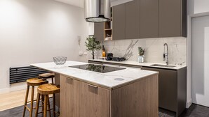 A modern kitchen with a central island, wooden stools, a marble backsplash, and a stainless steel faucet. - Waou Justice V - Short Term Rental (Madrid)