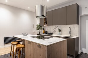 A modern kitchen with a central island, wooden stools, a marble backsplash, and a stainless steel faucet. - Waou Justice V - Short Term Rental (Madrid)