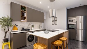A modern kitchen with a central island, bar stools, a washing machine, and a built-in oven. - Waou Justice V - Short Term Rental (Madrid)