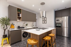 A modern kitchen with a central island, bar stools, a washing machine, and a built-in oven. - Waou Justice V - Short Term Rental (Madrid)