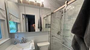 Een moderne badkamer met een douchecabine van glas, een wit toilet en een wastafel met een spiegel erboven.