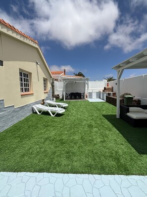 A backyard with artificial grass, a pergola, and a patio area with lounge chairs.