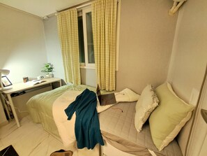 Une chambre à coucher comprenant un lit, un bureau, une chaise, une fenêtre avec des rideaux et une table de chevet avec une lampe et une plante.