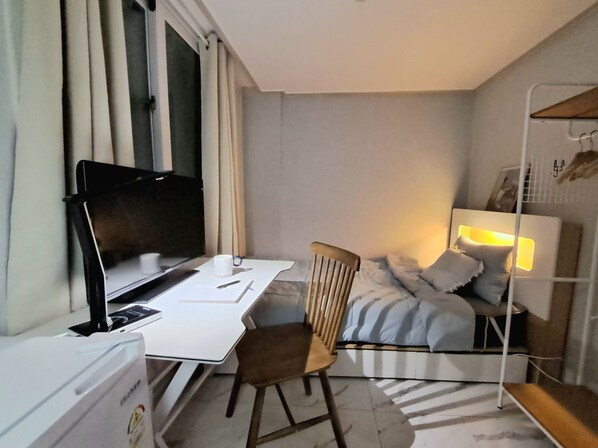 Une chambre d’hôtel de taille réduite, comprenant un lit, un bureau avec un ordinateur, une chaise et une lampe de chevet.