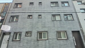 A multi-story building with a brick facade, multiple windows, and a visible entrance with a door. - Dodahm Guesthouse (Incheon)