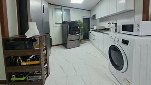 A modern kitchen with white cabinets, a washing machine, a microwave, and a refrigerator. - Dodahm Guesthouse (Incheon)