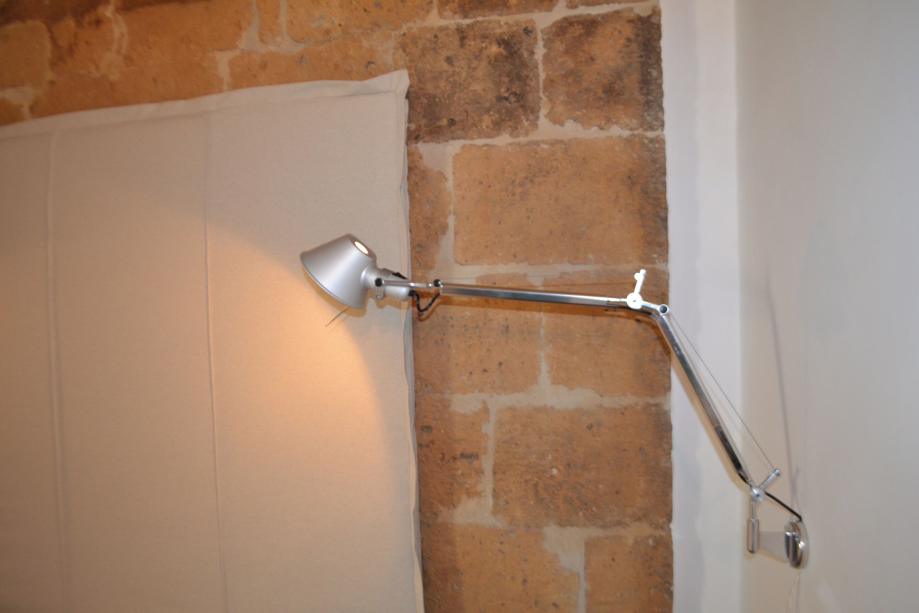 Een muurlamp met een flexibele arm, geplaatst tegen een bakstenen muur en een witte deur.