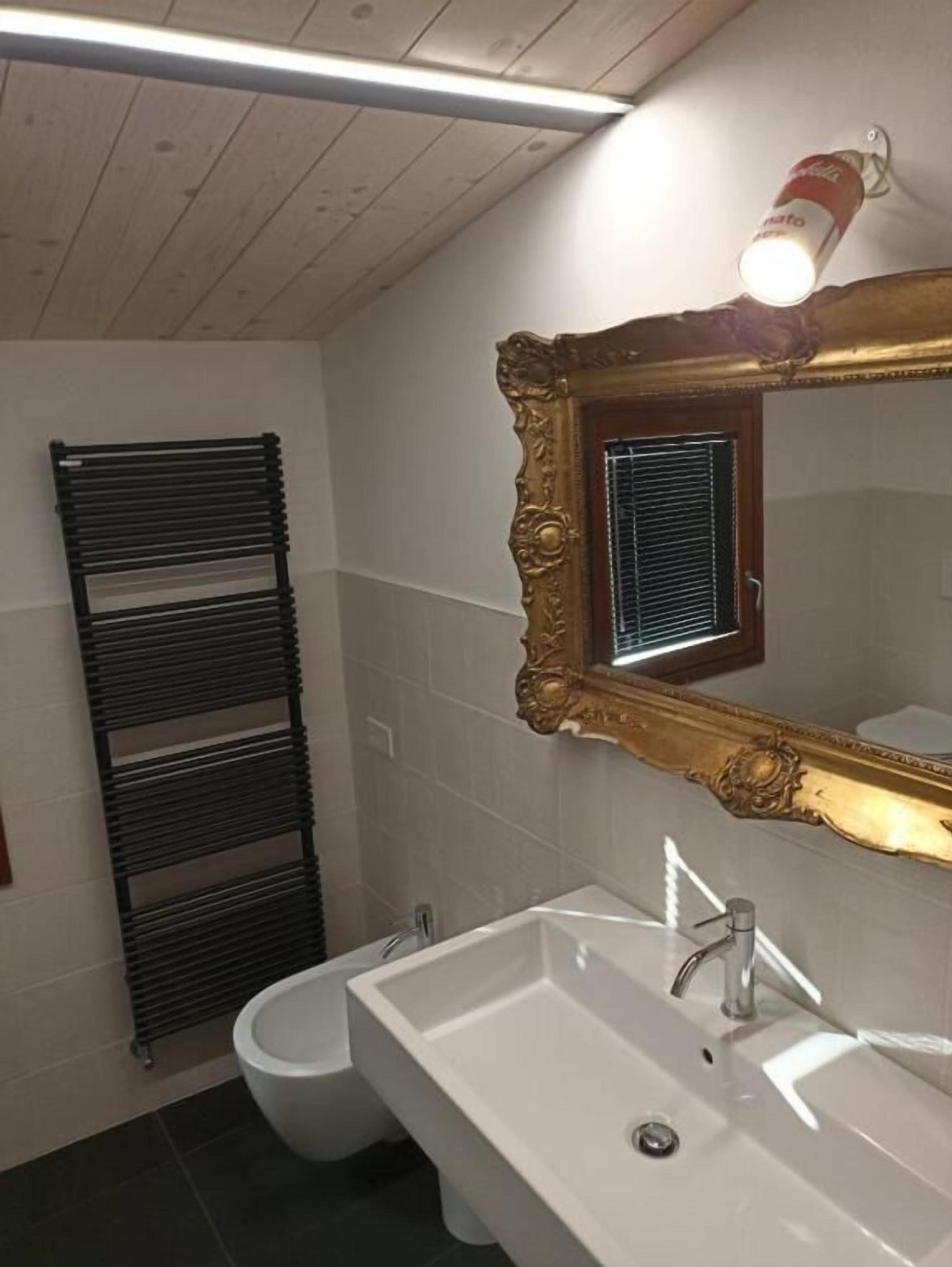 Ein Badezimmer mit Waschbecken, Toilette, schwarzem Heizkörper und einem Spiegel mit aufwendiger Rahmung.