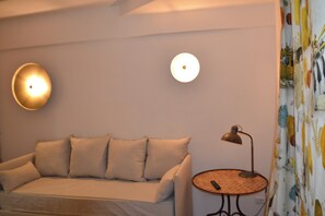 Une pièce avec un canapé beige, une petite table ronde avec une lampe et deux appliques murales.