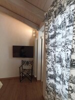 Una habitación con un televisor de pantalla plana en la pared, un sillón estampado y una cortina con un motivo natural.