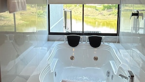 A modern bathroom with a large bathtub, a showerhead, and a window with a view of a lake.