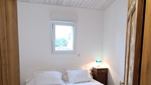 Quarto com teto de madeira, janela, mesa de cabeceira com abajur e cama com roupa de cama branca.