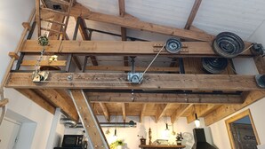 Interior rústico com vigas de madeira aparentes, sistema de polias e área de cozinha com eletrodomésticos e objetos decorativos.