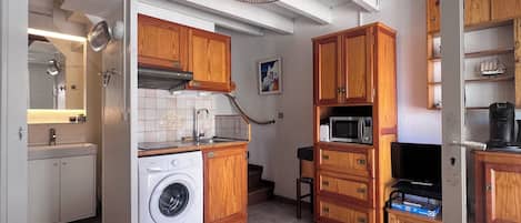A compact kitchen with wooden cabinets, a washing machine, a microwave, and a television.