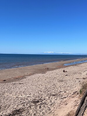 Ein Strand mit blauem Himmel, ruhiger See und fernen, schneebedeckten Bergen.