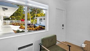 A modern room with a large window, a green chair, a small table, and a white door. - Chic 1-BD Apt in Miami Gym-Free Parking (North Miami)