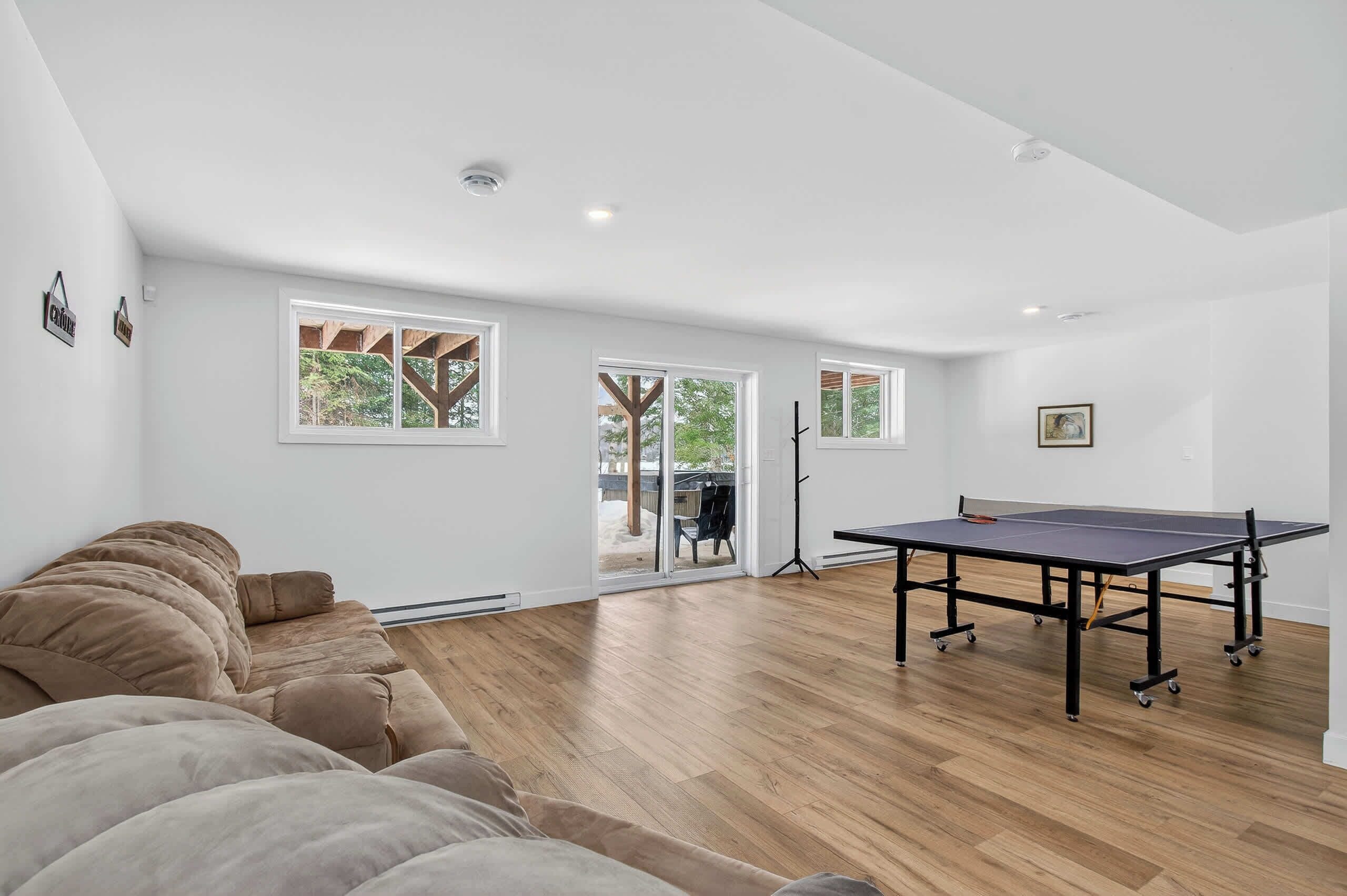 Una habitación amplia con mesa de ping pong, sofá y ventanas grandes.