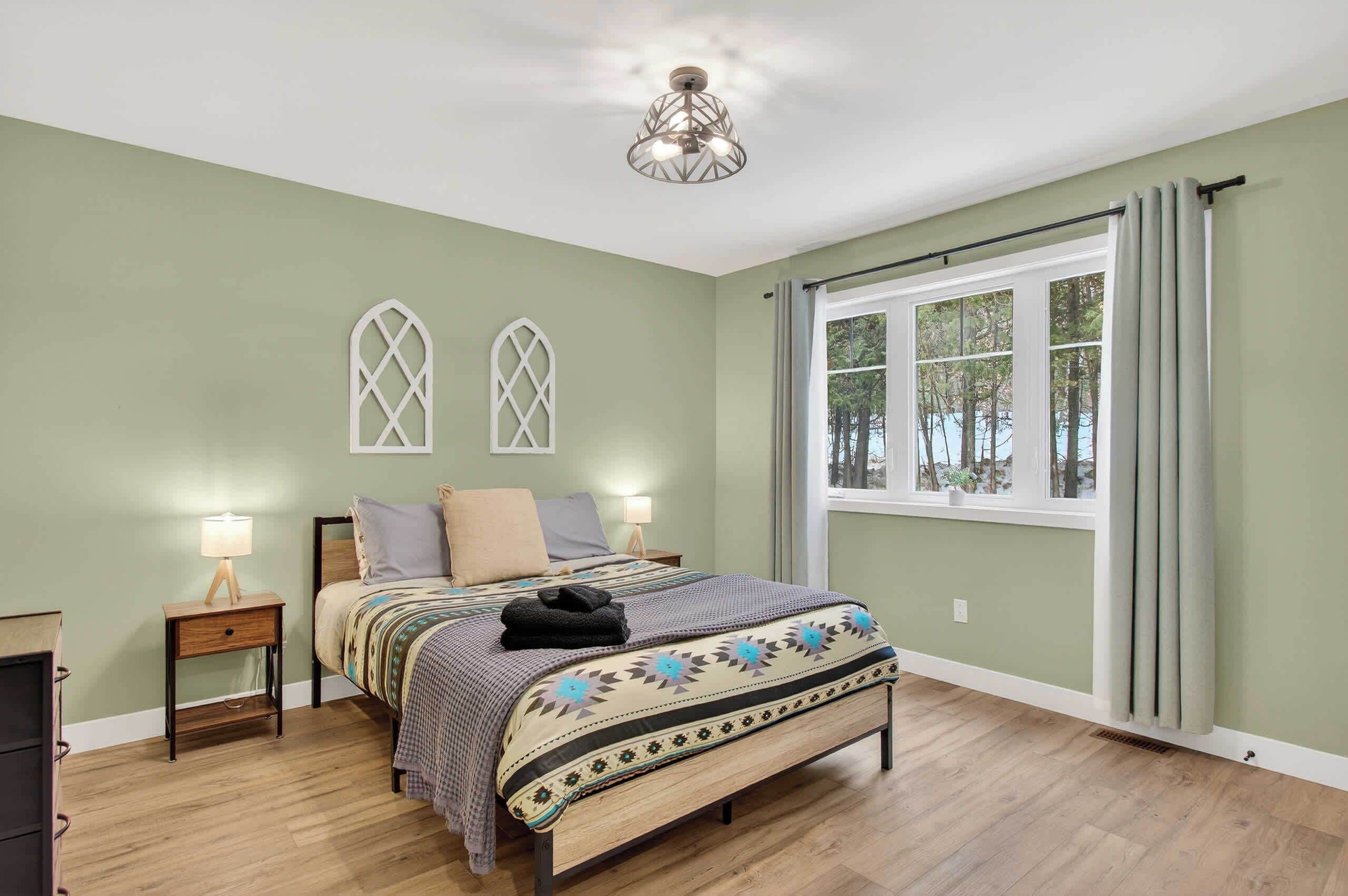 Un dormitorio con una cama, dos mesitas de noche con lámparas, una ventana con cortinas y una lámpara decorativa en el techo.